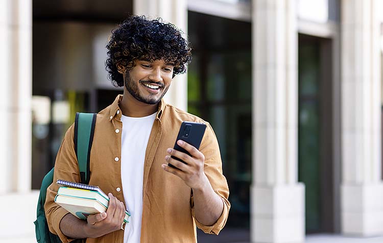 Young man holding books and looking at his phone