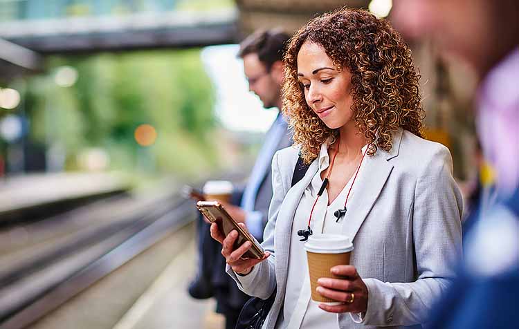 Woman at train station looking at phone holding a takeaway coffee