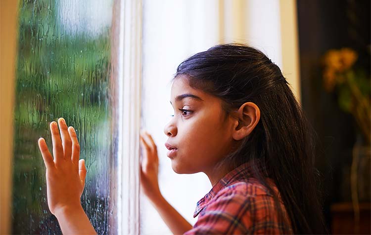 A cute little girl looking out the window on a rainy day.