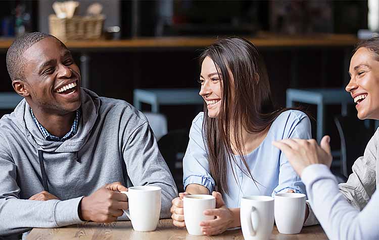 Three young adults laughing over coffee