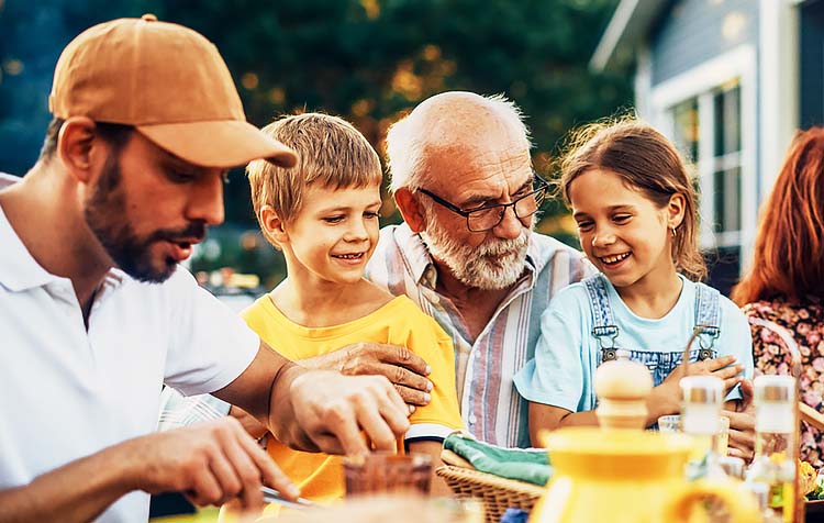 Father with two young children and grandfather eating outdoors at a picnic table.