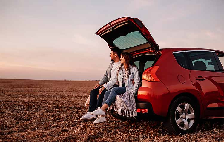 Couple sitting in back of car, looking at the sunset